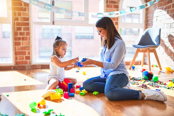 Caucasian girl kid playing and learning at playschool with female teacher. Mother and daughter at playroom around toys playing with bulding blocks - Photo, Image