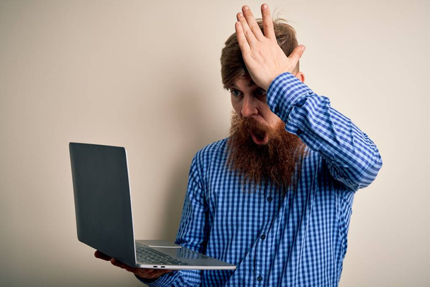 Redhead homme d'affaires irlandais avec barbe en utilisant ordinateur portable sur fond isolé stressé avec la main sur la tête, choqué par la honte et le visage surprise, en colère et frustré. Peur et contrariété par erreur
. - Photo, image