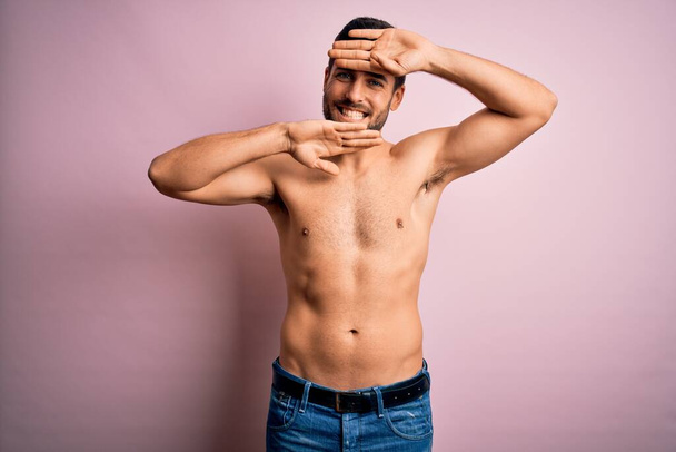 Young handsome strong man with beard shirtless standing over isolated pink background Smiling cheerful playing peek a boo with hands showing face. Surprised and exited - Фото, зображення