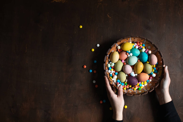 Easter background. Bowl with colored Easter eggs in women's hands. Space for text - Foto, Imagem