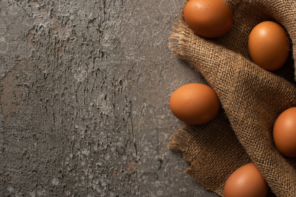 top view of brown eggs on sackcloth on grey textured background - Photo, Image