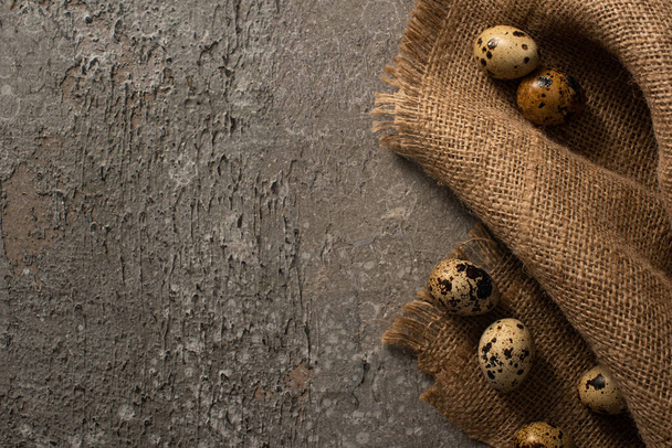 top view of quail eggs on sackcloth on grey textured background - Foto, afbeelding