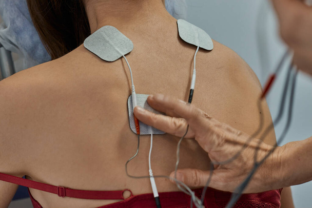 Electro stimulation in physical therapy to a young woman. Medical check at the shoulder in a physiotherapy center. Tens therapy - Photo, Image