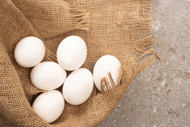 top view of white chicken eggs on sackcloth on grey concrete background - Zdjęcie, obraz