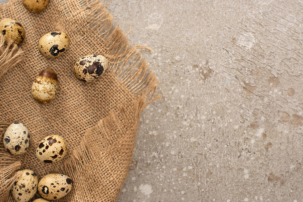 top view of quail eggs on sackcloth on grey cement background - Zdjęcie, obraz