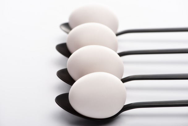 foco seletivo de ovos de galinha branca em colheres pretas no fundo branco
 - Foto, Imagem