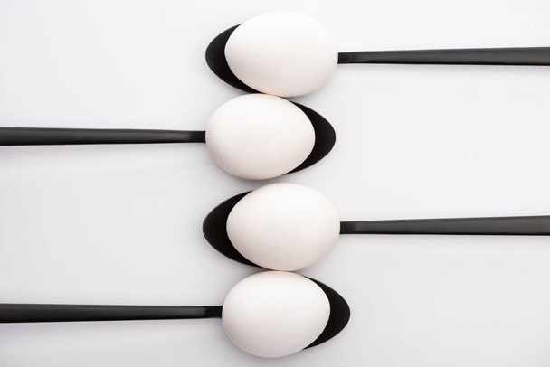 top view of white chicken eggs on black spoons on white background - Fotoğraf, Görsel