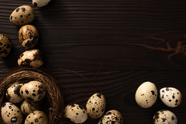 top view of quail eggs in nest and on dark wooden background - Zdjęcie, obraz