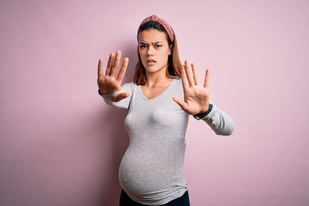 Fiatal gyönyörű tinédzser lány terhes vár baba felett elszigetelt rózsaszín háttér csinál stop gesztus kezével tenyér, dühös és frusztráció kifejezés - Fotó, kép