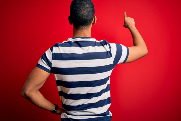Позивний афроамериканець у смугастій футболці, що стоїть над червоним фоном Позивний назад, спрямований вперед пальцем. - Фото, зображення