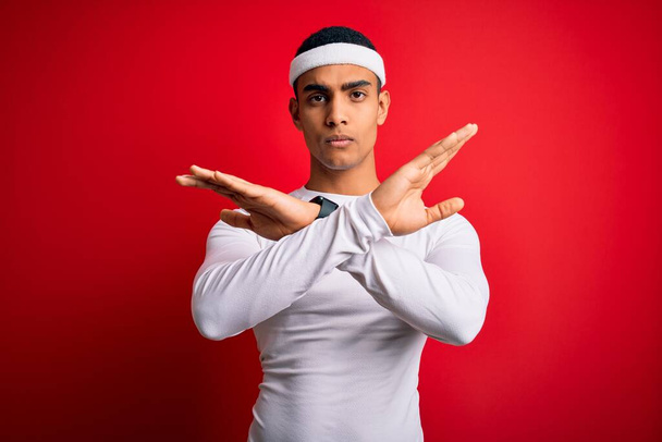 Young handsome african american sportsman wearing sportswear over red background Rejection expression crossing arms doing negative sign, angry face - 写真・画像