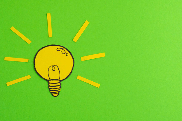 切り紙で構成され、緑の背景に電球を描きます。アイデアを象徴する創造的なコンセプト. - 写真・画像