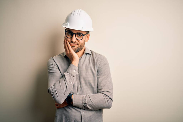 Young architect man wearing builder safety helmet over isolated background thinking looking tired and bored with depression problems with crossed arms. - Fotografie, Obrázek