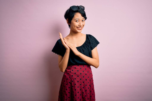 Junge schöne asiatische Mädchen in lässigem Kleid stehen über isolierten rosa Hintergrund klatschen und applaudieren glücklich und fröhlich, lächeln stolze Hände zusammen - Foto, Bild