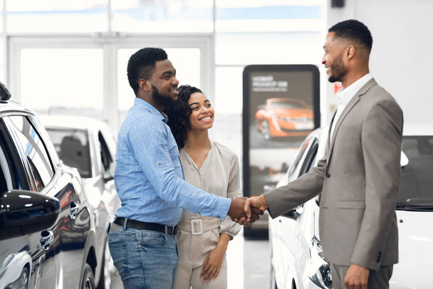 Car Dealer Handshaking With Buyers After Successful Deal In Store - Фото, изображение
