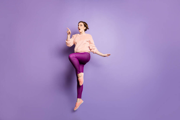 OMG. Full length photo of pretty lady jumping up high looking low shopping prices directing finger advert banner wear casual fluffy stylish pullover pants isolated purple color background - Foto, Imagem