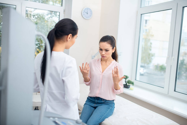 Dark-haired woman wearing jeans speaking with plastic surgeon - Foto, Imagem