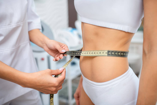 Close up of doctor measuring waistline of slim patient - Foto, Imagen