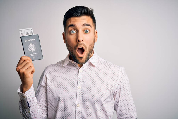 Молодой красивый турист, держащий паспорт США с долларами напуганный в шоке с неожиданным лицом, напуганный и взволнованный выражением страха
 - Фото, изображение