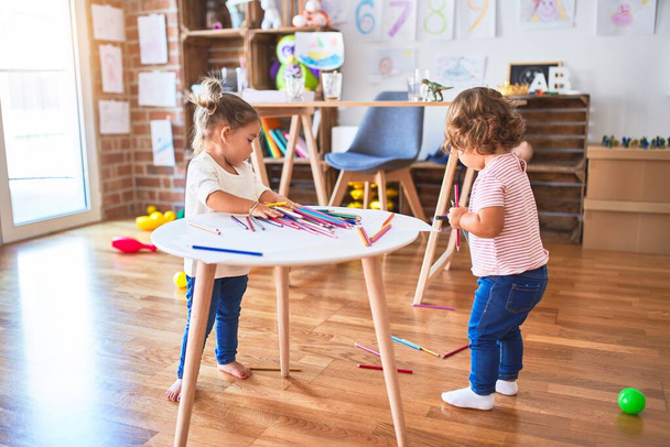 Imádnivaló kisgyermekek játszanak sok színes ceruzával az asztalon az óvodában - Fotó, kép