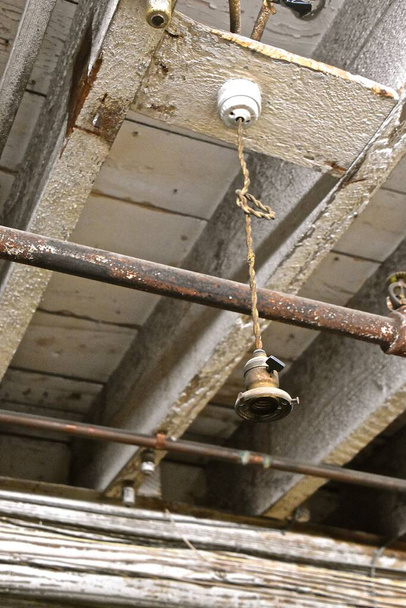 A very old electrical lighting receptacle hangs from the joices of a warehouse - Photo, Image