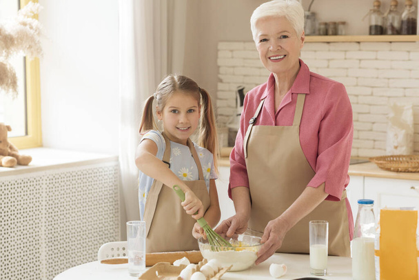 Happy granny and her granddaughter baking togeher in kitchen, copy space - Foto, afbeelding