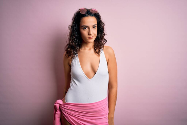 Beautiful woman with curly hair on vacation wearing white swimsuit over pink background looking sleepy and tired, exhausted for fatigue and hangover, lazy eyes in the morning. - Photo, Image