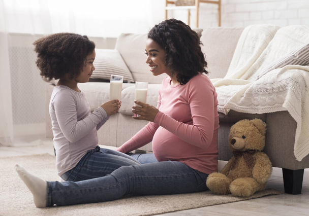 Pieni afro tyttö ja hänen raskaana oleva äitinsä juovat maitoa kotona
 - Valokuva, kuva