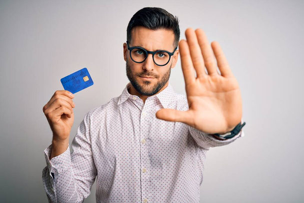 Nuori liikemies jolla luottokortti yli eristetty tausta avoimin käsin tekee stop merkki vakava ja luottavainen ilme, puolustus ele
 - Valokuva, kuva