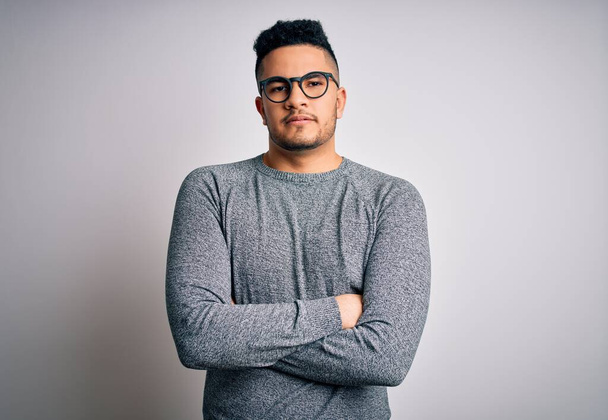 Young handsome man wearing casual sweater and glasses over isolated white background skeptic and nervous, disapproving expression on face with crossed arms. Negative person. - Photo, Image