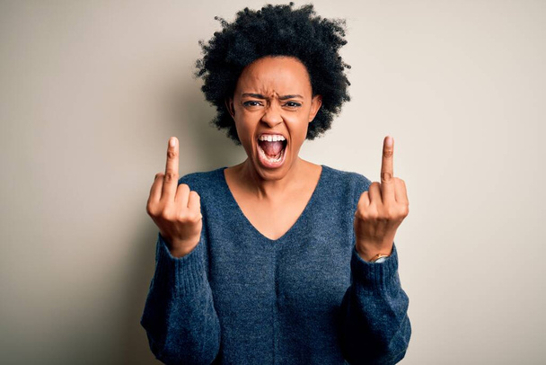 Young beautiful African American afro woman with curly hair wearing casual sweater Showing middle finger doing fuck you bad expression, provocation and rude attitude. Screaming excited - Zdjęcie, obraz