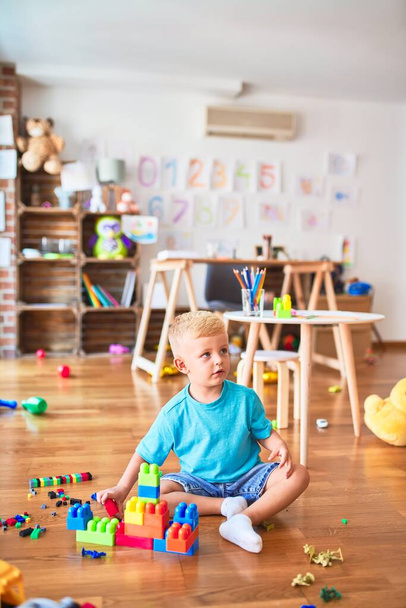 Young caucasian kid playing at kindergarten with toys blocks. Preschooler boy happy at playroom building a tower - Zdjęcie, obraz