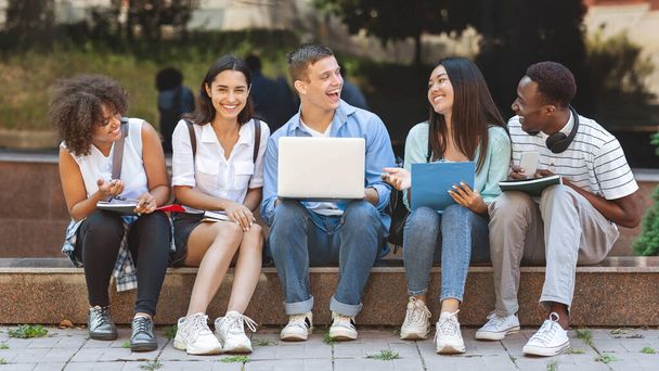 Студенты счастливого университета сидят в кампусе с ноутбуком и смеются вместе
 - Фото, изображение