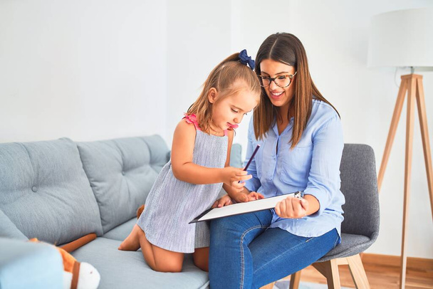 Young therapist woman speaking and treating child, counselor and behaviour correction at pedagogue payroom taking notes on clipboard - Photo, Image