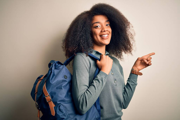 Junge afrikanisch-amerikanische Studentin mit Afro-Haaren trägt Rucksack über dem Hintergrund sehr glücklich zeigt mit Hand und Finger zur Seite - Foto, Bild