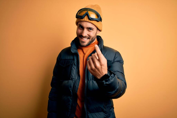 Jeune homme beau skieur barbu portant des vêtements de sport de neige et des lunettes de ski Beckoning venir ici geste avec la main invitant accueillant heureux et souriant
 - Photo, image