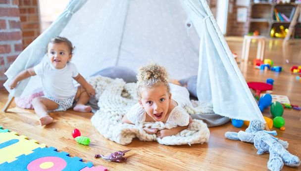 Beautiful toddlers playing inside tipi over blanket around lots of toys at kindergarten - Foto, Imagem