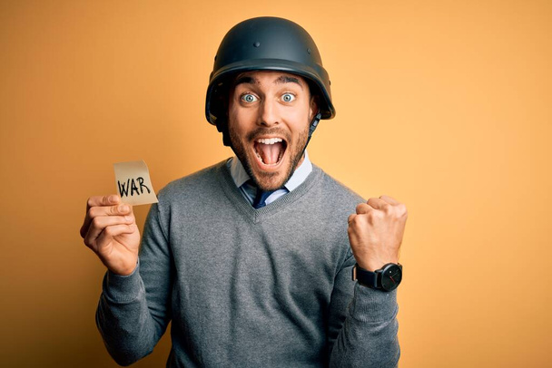 Beau homme d'affaires portant un casque militaire tenant papier de rappel avec message de guerre criant fier et célébrant la victoire et le succès très excité, acclamant l'émotion
 - Photo, image