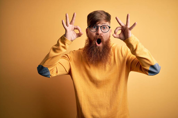 Bello irlandese rossa uomo con barba indossare occhiali su sfondo giallo isolato cercando sorpreso e scioccato facendo ok simbolo di approvazione con le dita. Espressione folle
 - Foto, immagini