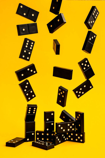 Black Dominoes flying on yellow background, Closeup scattered dominoes on a yellow Board game, Game night Dominos table game - Фото, изображение