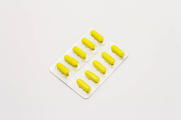 Pharmaceutical tablets, yellow capsules in blister pack isolated on white background. Treatment of various diseases, traditional medicine - Foto, imagen