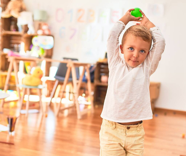 美しいブロンドの幼児は幸せな保持ボールを笑っています。幼稚園のおもちゃの周りに立って - 写真・画像