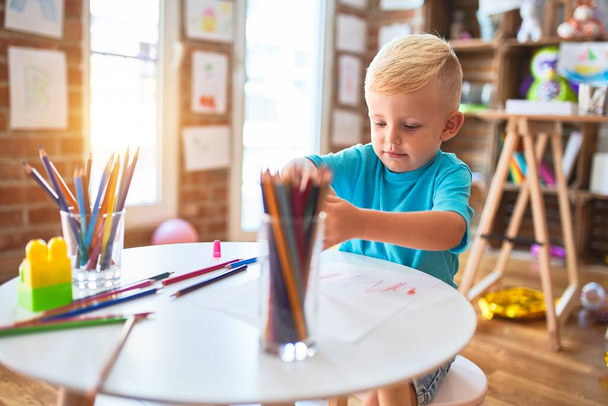 Fiatal kaukázusi gyerek, aki az óvodában rajzol színes ceruzákkal. Az óvodás fiú boldog a játszószobában.. - Fotó, kép