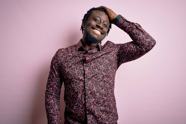Jeune bel homme afro-américain portant une chemise décontractée debout sur fond rose souriant confiant toucher les cheveux avec geste de la main vers le haut, posant attrayant et à la mode
 - Photo, image