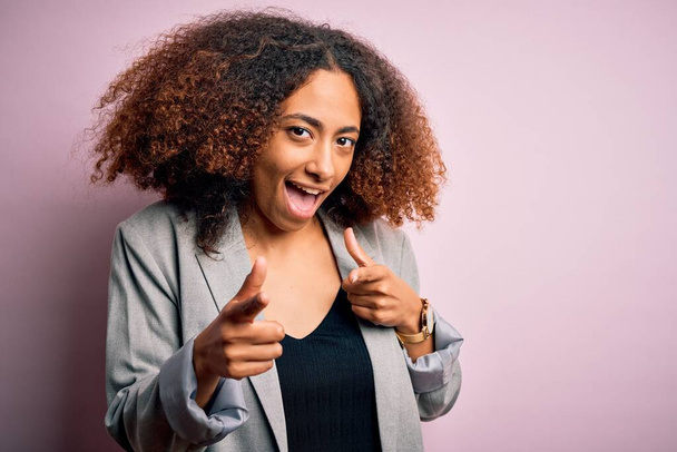 Young african american businesswoman with afro hair wearing elegant jacket pointing fingers to camera with happy and funny face. Good energy and vibes. - Zdjęcie, obraz
