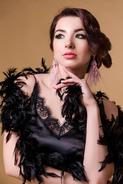 beautiful brunette sensitive woman in boa from ostrich feathers is posing on beige background. Vertycal photo - 写真・画像