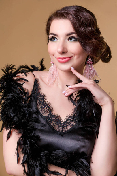 beautiful brunette  woman in boa from ostrich feathers is posing and smiling on beige background. Vertycal photo - Photo, Image