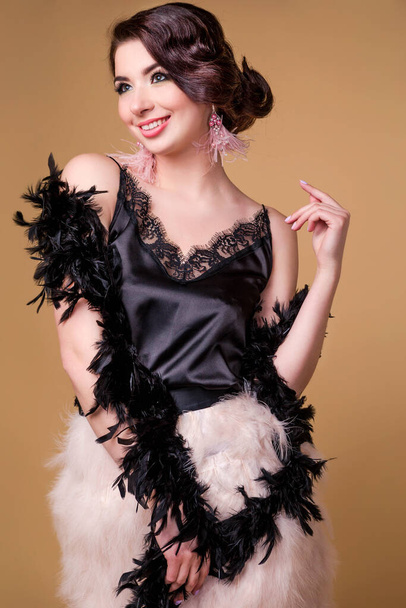 beautiful brunette  woman in boa from ostrich feathers is posing and smiling on beige background. Vertycal photo - Фото, зображення