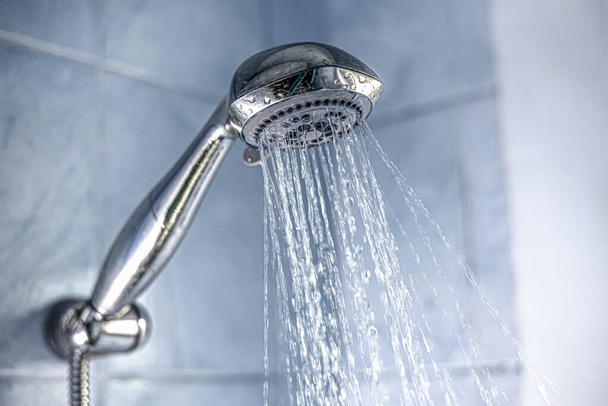 Gümüş bir duş başlığının banyoya su sıçratması. - Fotoğraf, Görsel