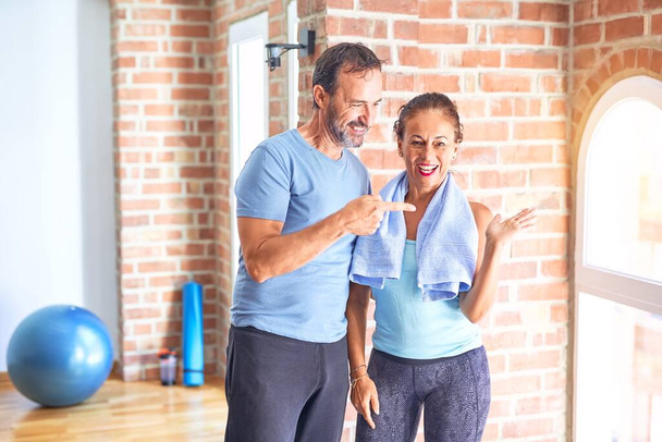Middle age sporty couple standing before do exercise at gym amazed and smiling to the camera while presenting with hand and pointing with finger. - Φωτογραφία, εικόνα